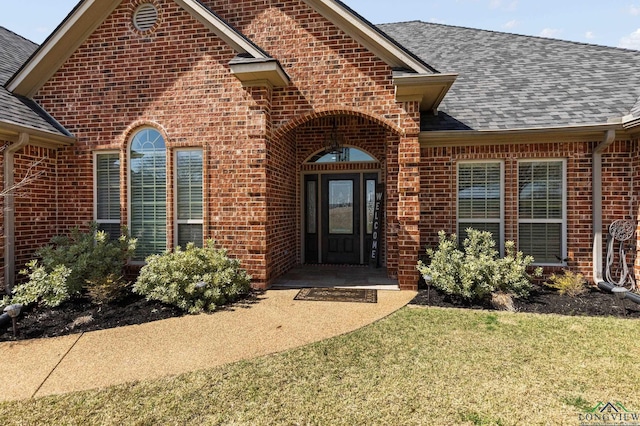 view of exterior entry featuring brick siding and a shingled roof