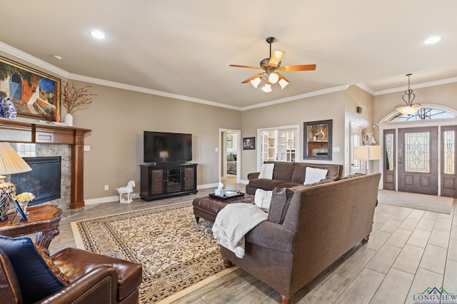 living room with baseboards, light wood-style flooring, ceiling fan, ornamental molding, and a tile fireplace