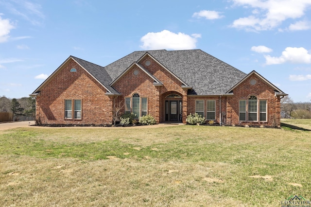 view of front of property featuring brick siding, a front yard, and a shingled roof