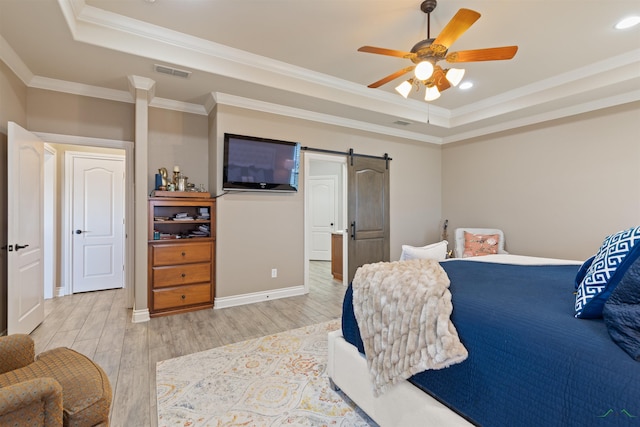 bedroom featuring a tray ceiling, a barn door, visible vents, and light wood finished floors