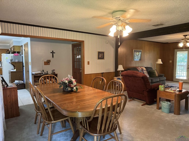 carpeted dining area featuring ceiling fan, ornamental molding, a textured ceiling, and wooden walls