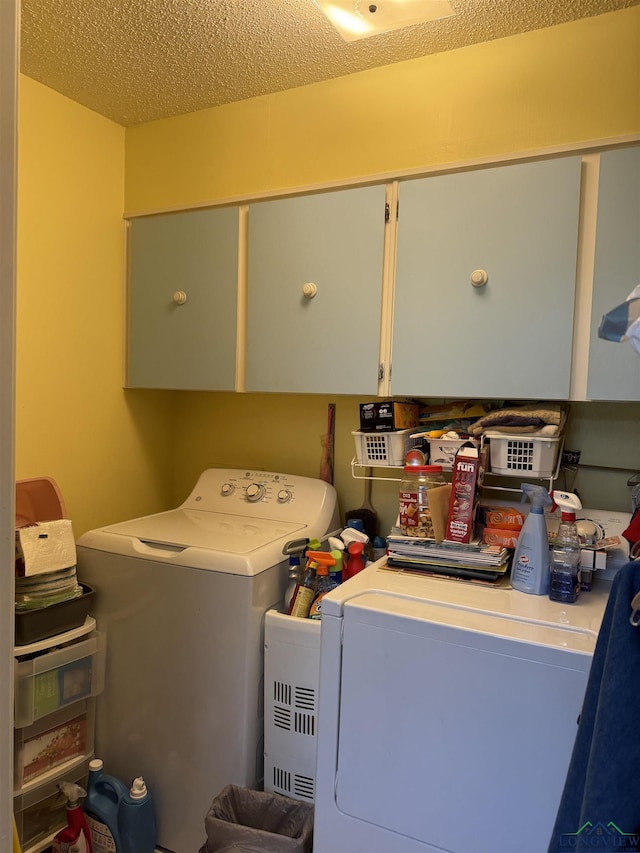 clothes washing area with washer and dryer, a textured ceiling, and cabinets