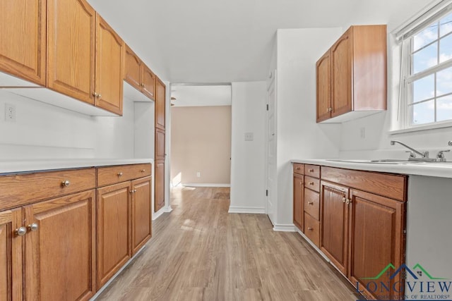 kitchen with baseboards, light wood finished floors, a sink, light countertops, and brown cabinets