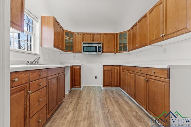 kitchen featuring stainless steel microwave, light wood-style flooring, glass insert cabinets, and brown cabinets