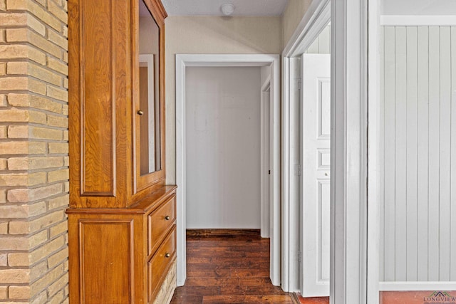 hall with dark wood-type flooring and brick wall