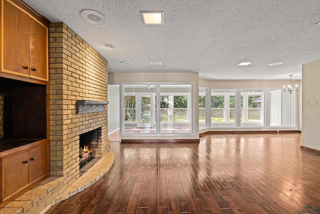 unfurnished living room with a textured ceiling, hardwood / wood-style floors, a fireplace, and an inviting chandelier