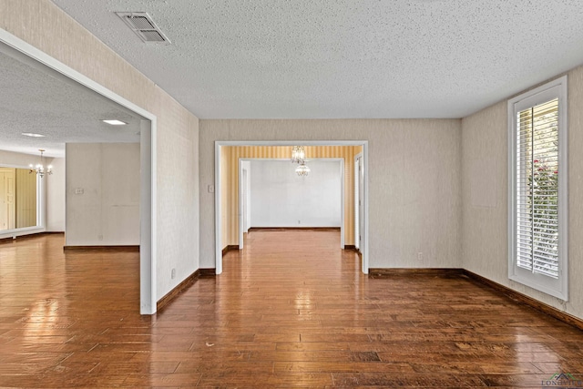 empty room featuring dark wood-type flooring, a textured ceiling, and a notable chandelier