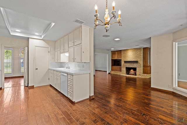 kitchen featuring white cabinetry, dark hardwood / wood-style flooring, white dishwasher, and a brick fireplace