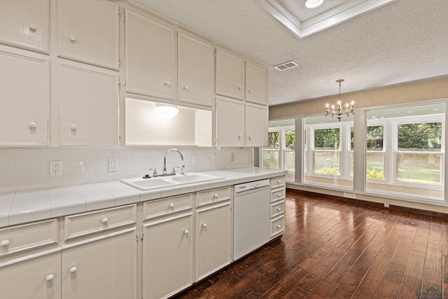 kitchen with tile countertops, dishwasher, sink, hanging light fixtures, and decorative backsplash