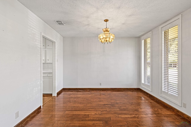 spare room with dark wood-type flooring, a textured ceiling, and a notable chandelier