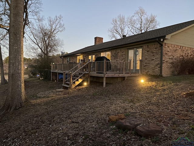 back of house with roof with shingles, a wooden deck, a chimney, and brick siding