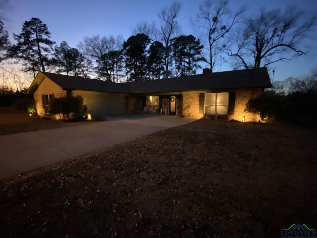 ranch-style house featuring driveway, a chimney, and stone siding