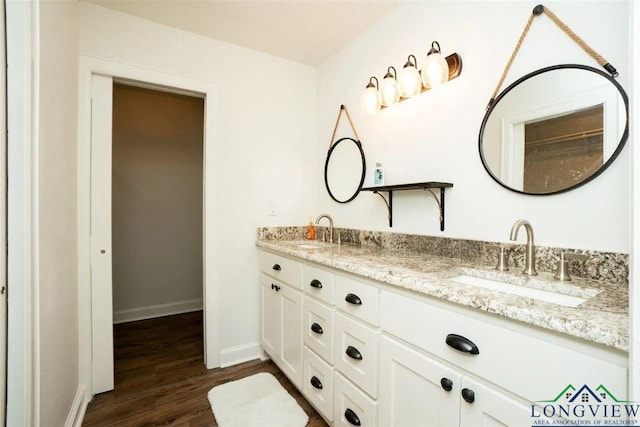 bathroom featuring a sink, baseboards, double vanity, and wood finished floors