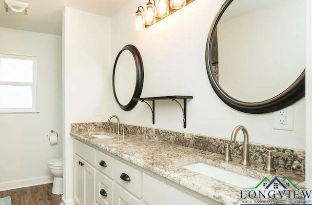 full bathroom with a sink, double vanity, toilet, and wood finished floors