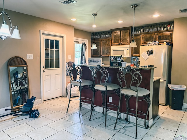 203 Reynolds St, Pittsburg, TX 75686 - kitchen with white appliances, dark brown cabinetry, light tile patterned floors, a breakfast bar area, and pendant lighting