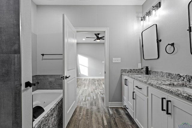 bathroom with hardwood / wood-style floors, vanity, ceiling fan, and tiled tub