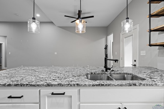 kitchen featuring sink, hanging light fixtures, ceiling fan, light stone countertops, and white cabinetry