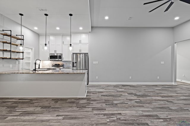 kitchen with white cabinets, ceiling fan, light stone countertops, appliances with stainless steel finishes, and wood-type flooring