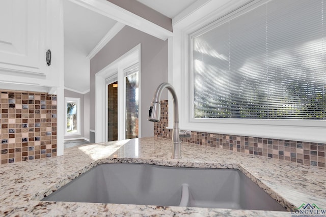 kitchen featuring a healthy amount of sunlight, light stone counters, ornamental molding, and sink