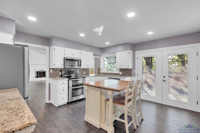 kitchen with a wealth of natural light, a center island, white cabinets, and appliances with stainless steel finishes