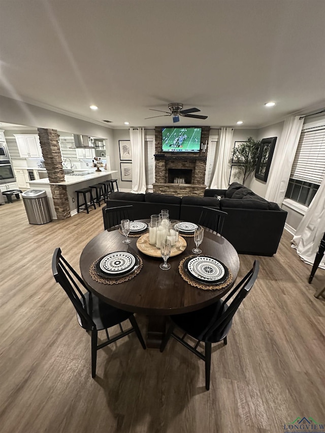 dining space with wood-type flooring, ceiling fan, and a fireplace