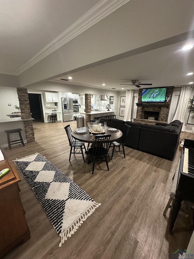 dining room featuring crown molding, hardwood / wood-style flooring, ceiling fan, a fireplace, and ornate columns