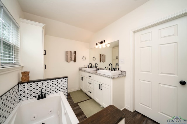 bathroom with a whirlpool tub, wood finished floors, lofted ceiling, and a sink