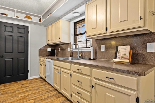 kitchen with dark countertops, decorative backsplash, white dishwasher, a sink, and light wood-type flooring