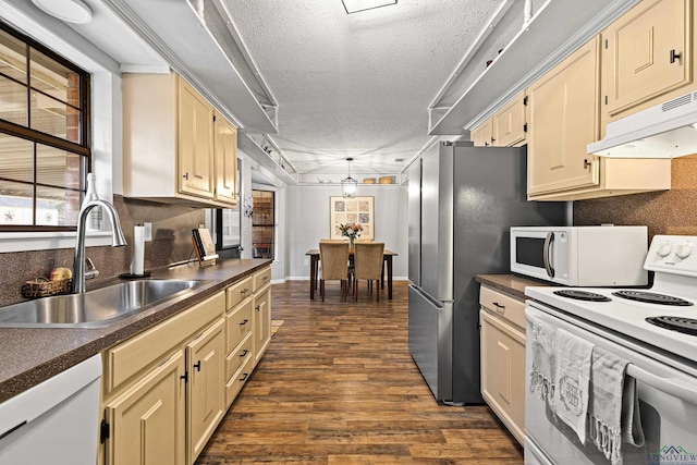 kitchen featuring dark wood finished floors, dark countertops, a sink, white appliances, and under cabinet range hood