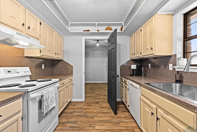 kitchen featuring white appliances, dark wood finished floors, dark countertops, under cabinet range hood, and a sink