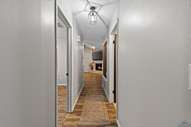 corridor featuring baseboards, dark wood finished floors, a textured ceiling, and a textured wall