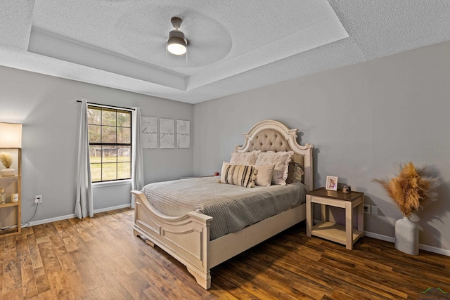 bedroom with baseboards, a tray ceiling, dark wood finished floors, and a textured ceiling