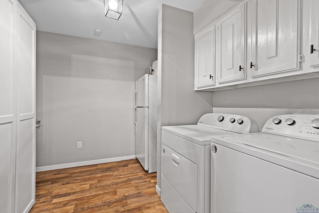 laundry area with cabinet space, a textured ceiling, wood finished floors, washer and dryer, and baseboards