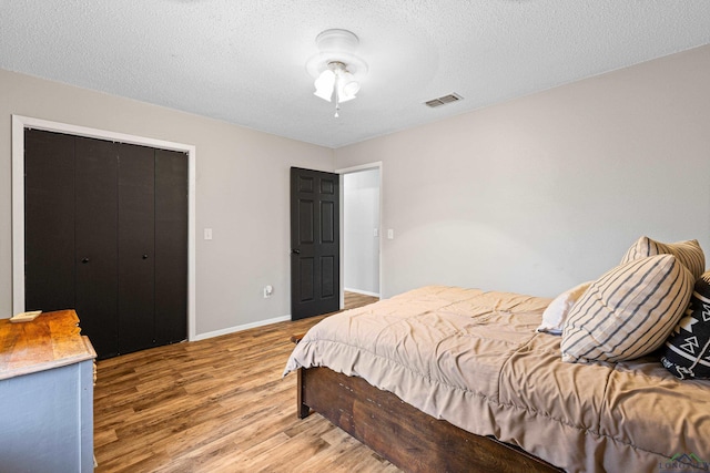 bedroom with a textured ceiling, wood finished floors, visible vents, and baseboards