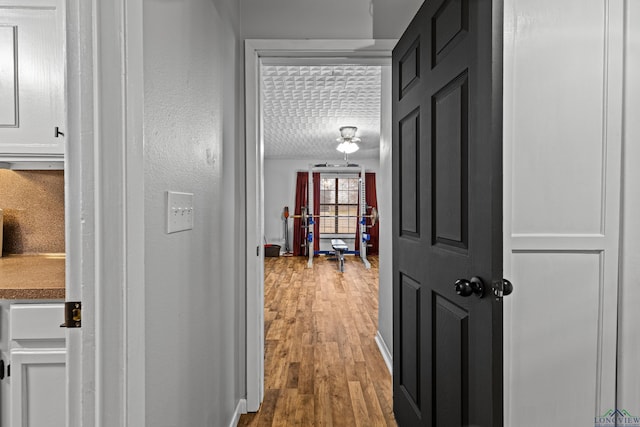 hall featuring a textured ceiling, baseboards, and wood finished floors