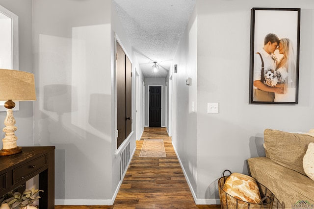 hallway with dark wood-style floors, baseboards, and a textured ceiling