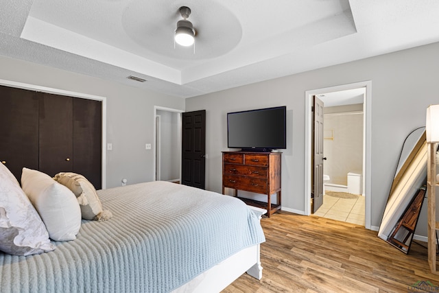 bedroom with a textured ceiling, visible vents, baseboards, a tray ceiling, and light wood finished floors