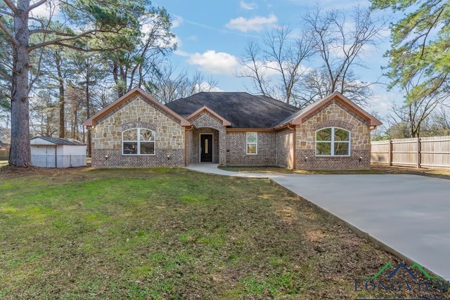 french country inspired facade with fence, driveway, roof with shingles, a front lawn, and an outdoor structure