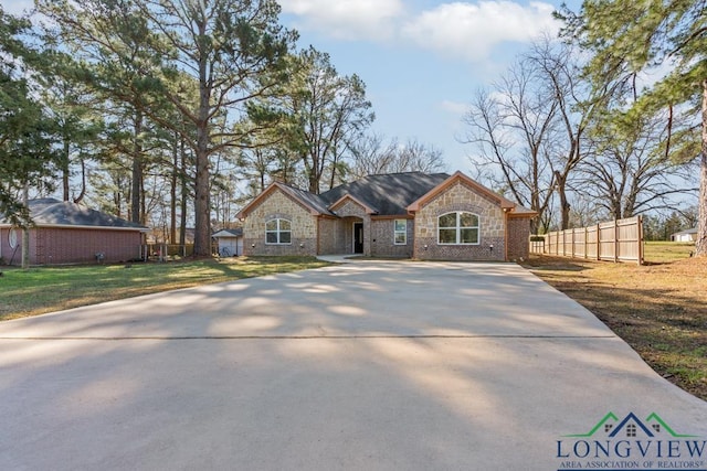 view of front facade featuring a front lawn, fence, stone siding, and driveway