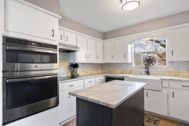 kitchen featuring sink, tasteful backsplash, a center island, white cabinets, and black appliances