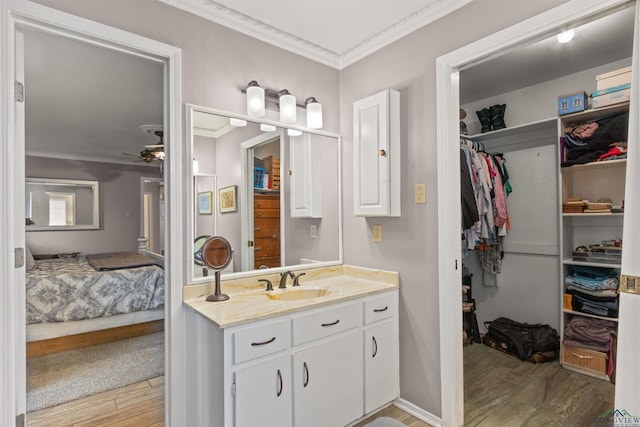 bathroom featuring ceiling fan, ornamental molding, wood-type flooring, and vanity