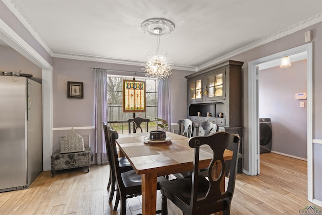 dining space with ornamental molding, washer / dryer, light hardwood / wood-style flooring, and a notable chandelier