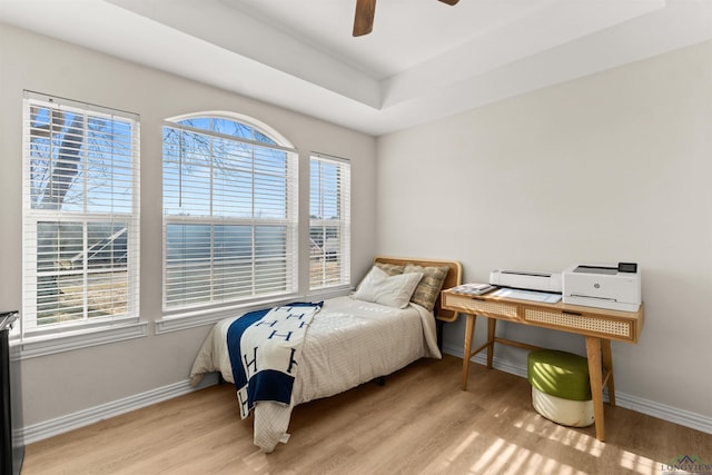 bedroom featuring ceiling fan, a raised ceiling, and light hardwood / wood-style floors