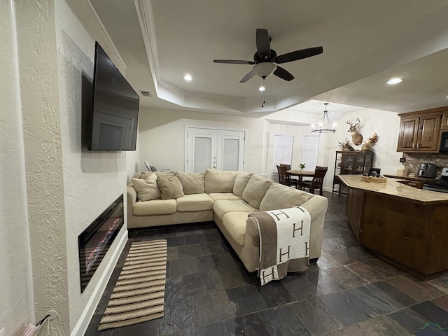 living room with ceiling fan with notable chandelier and a tray ceiling