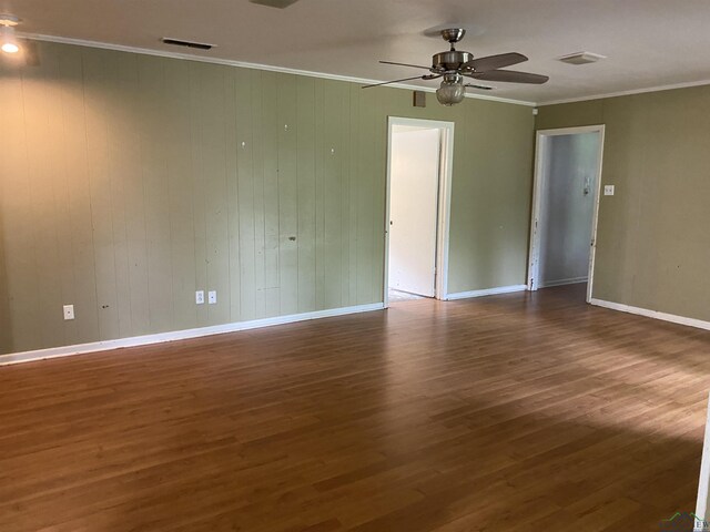 empty room featuring crown molding, a ceiling fan, wood finished floors, baseboards, and visible vents