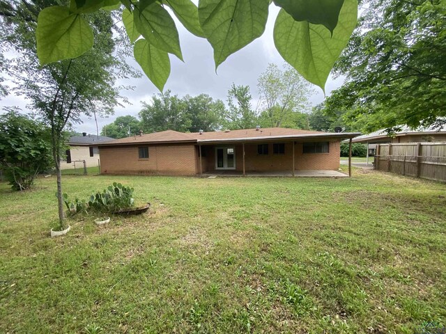 rear view of house with brick siding, a yard, a patio, and fence