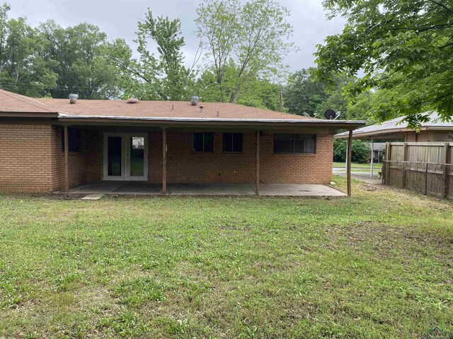 rear view of property featuring fence, a lawn, brick siding, and a patio
