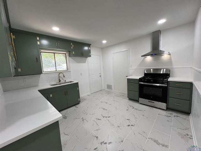 kitchen with backsplash, green cabinets, sink, stainless steel gas range, and wall chimney exhaust hood