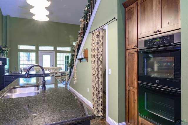 kitchen featuring black double oven, dark stone countertops, and sink