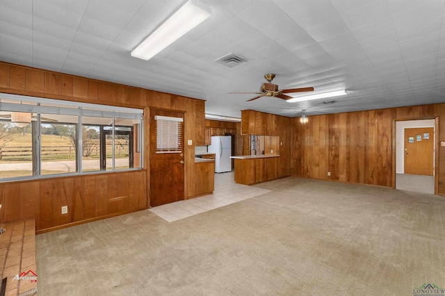 unfurnished living room featuring ceiling fan, light colored carpet, and wooden walls